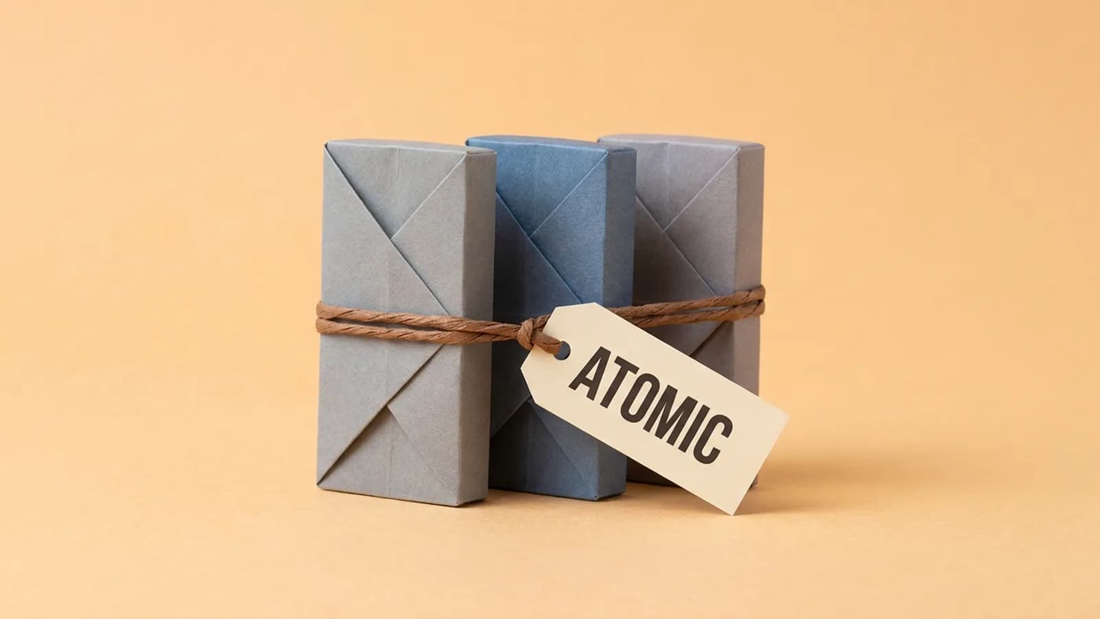 Three paper blocks tied together with one string and a tag reading ATOMIC, so they stand or fall as one